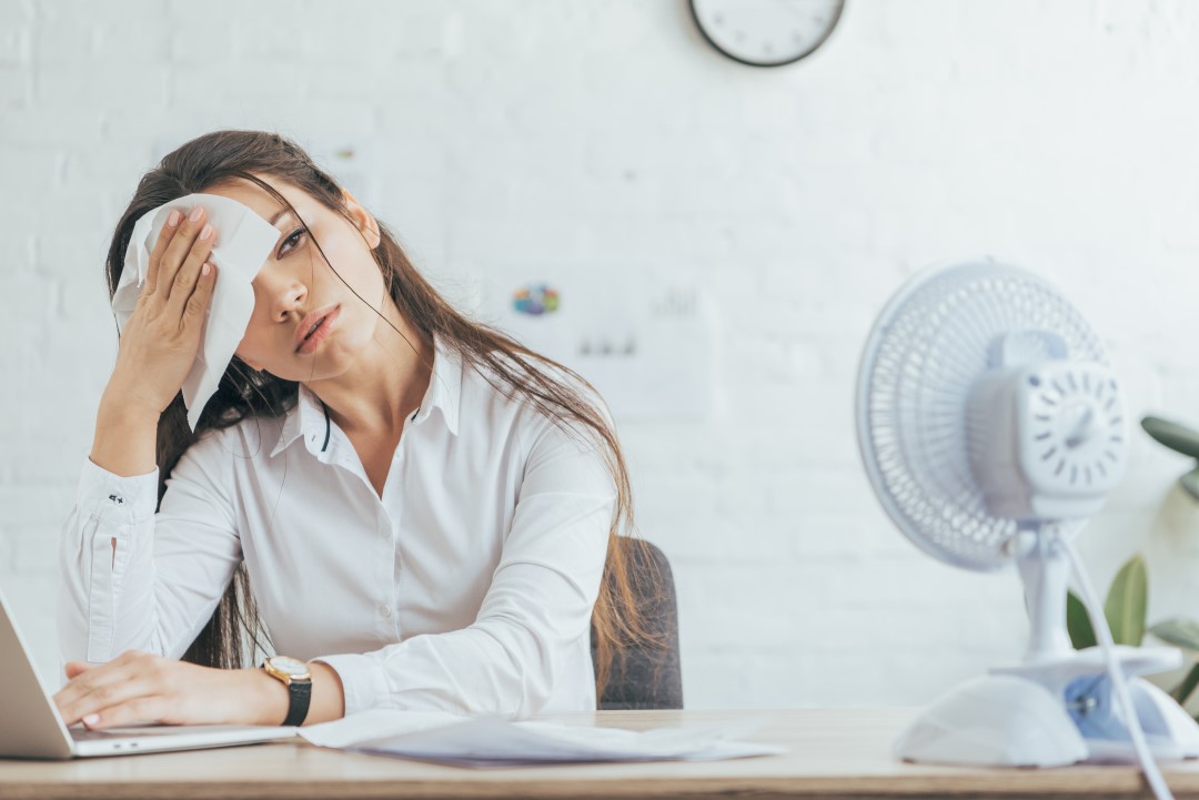 Woman sweating at home with a broken air conditioner in need of repair
